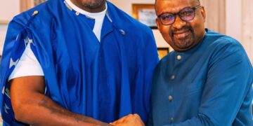 Two people smiling and shaking hands indoors.