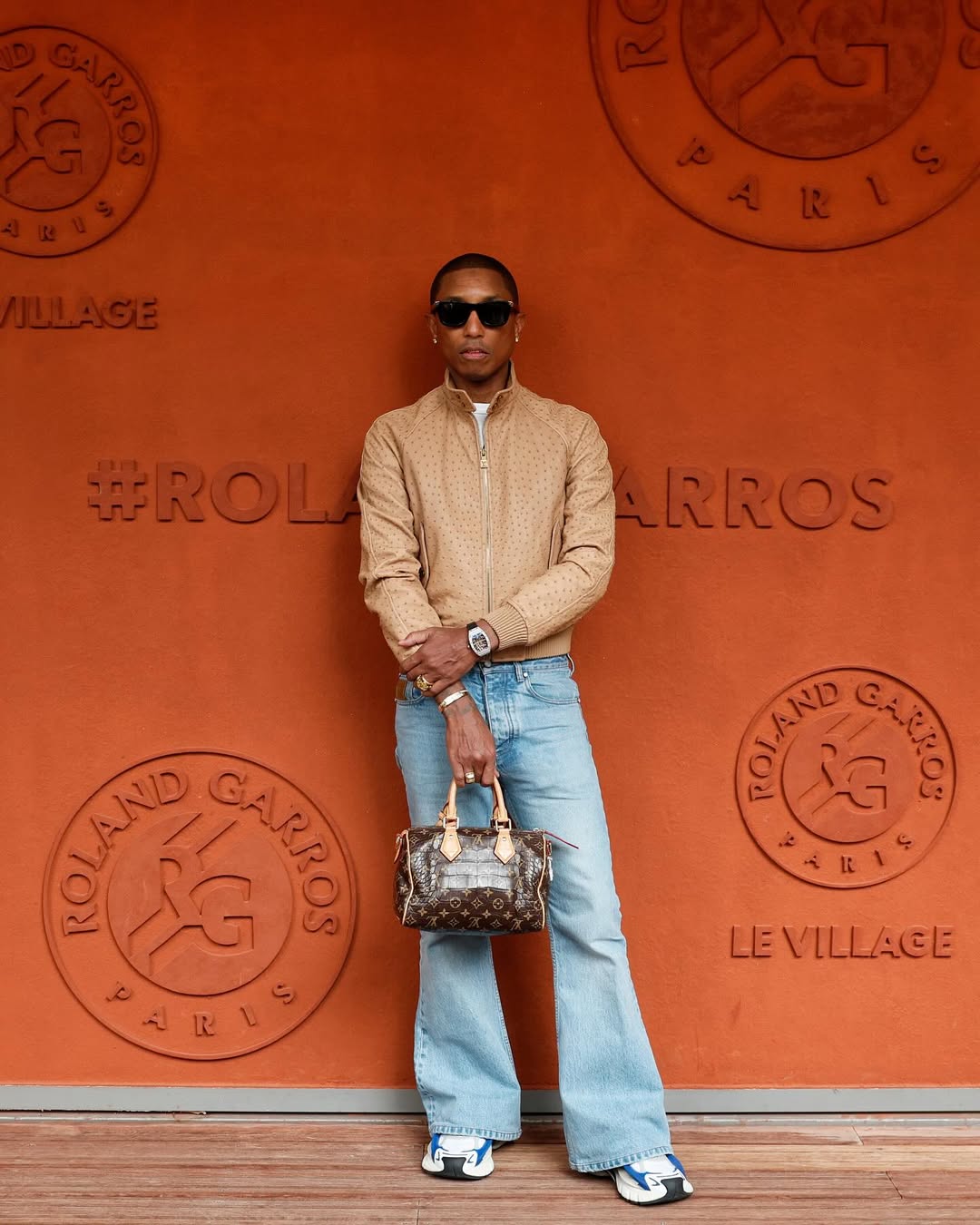 pharrell wearing brown jacket and bell bottom jeans