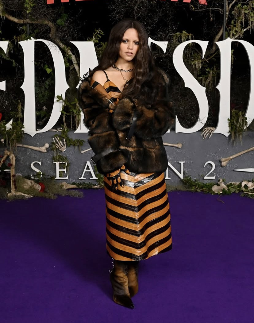 Jenna Ortega in striped leather dress with fur coat and spiked boots