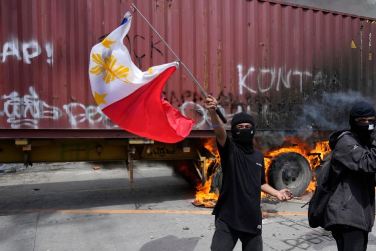A protester waves a Philippine flag beside a burning truck following clashes with police as they tried to enter the Malacanang presidential palace compound in Manila, Philippines on Sunday, Sept. 21, 2025. (AP Photo/Aaron Favila)