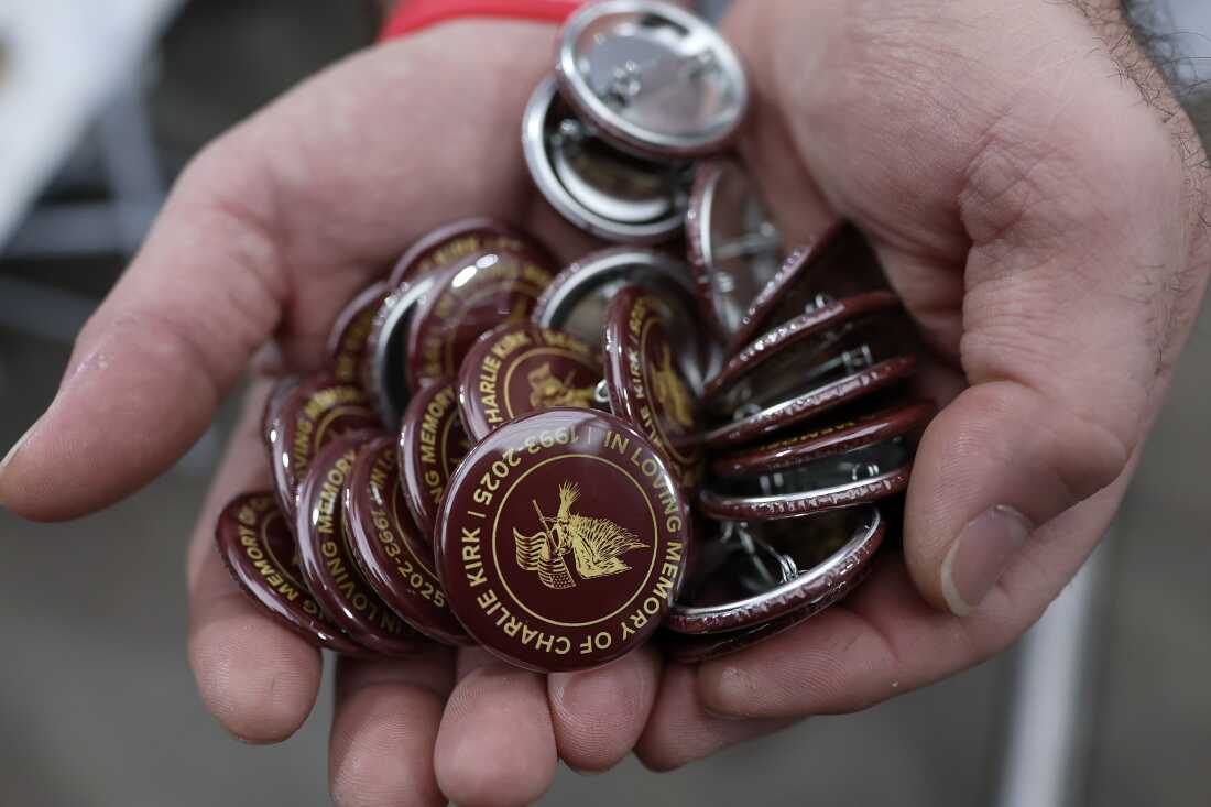Man displaying pins in memory of Charlie Kirk at memorial service