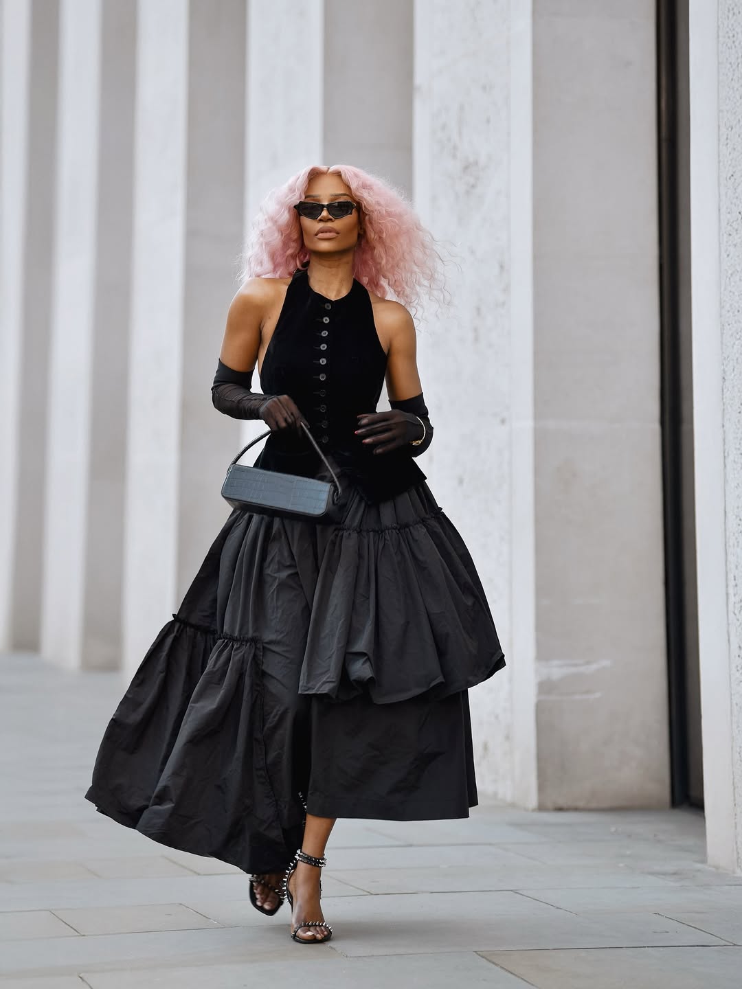 woman wearing black skirt with matching vest, small bag, and black sandals