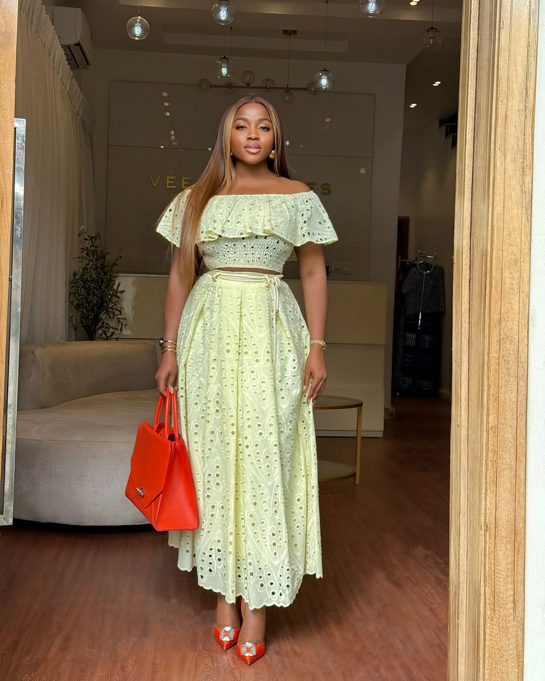 woman wearing yellow lace skirt set with orange leather tote bag and matching shoes