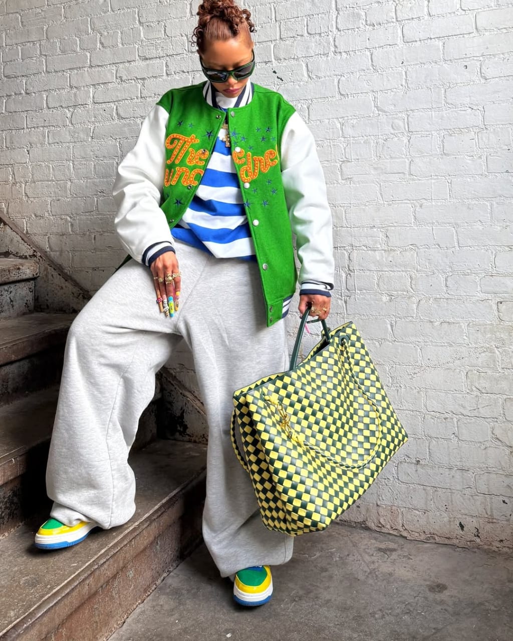 woman wearing green letterman jacket with joggers and large leather tote with sneakers
