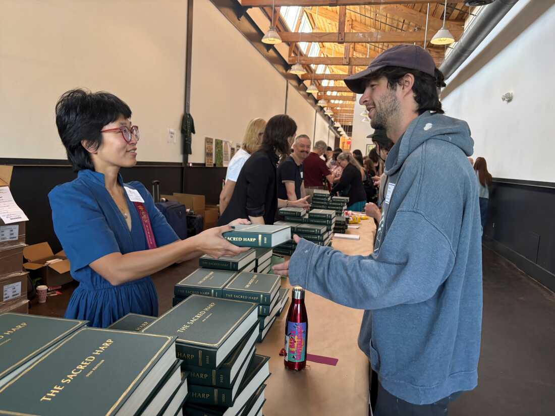 Leigh Cooper from San Francisco hands out the 2025 edition of The Sacred Harp at the convention entrance.