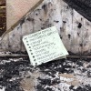 A sign with the names of church rooms and arrows pointing which way to go sits among burned ash and remains.
