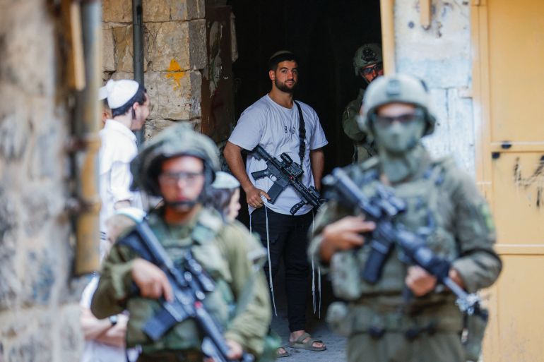 An armed settler stands near Israeli troops during a weekly settlers' tour in Hebron, West Bank