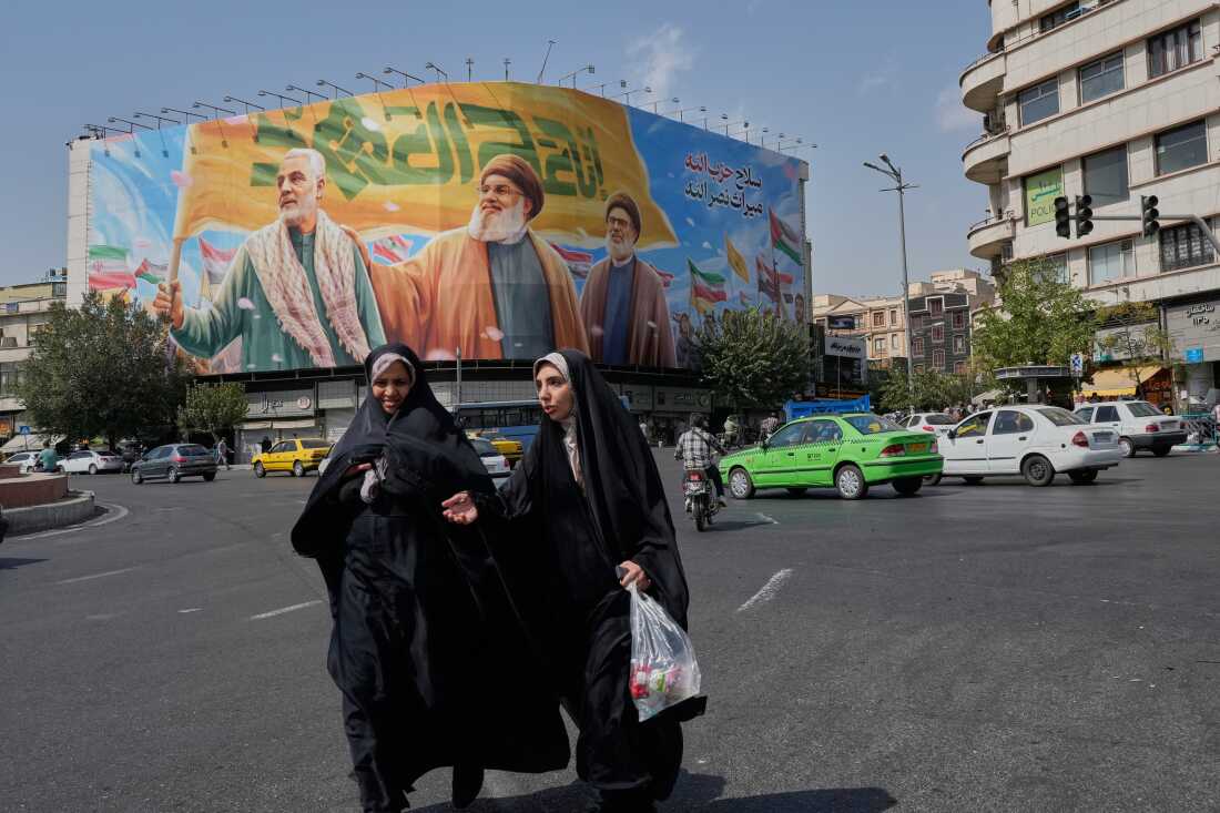 Two women walk past a large banner depicting Iran's Revolutionary Guard commander Qassem Soleimani and Hezbollah leaders killed in recent strikes, Tehran, Sept. 27, 2025.
