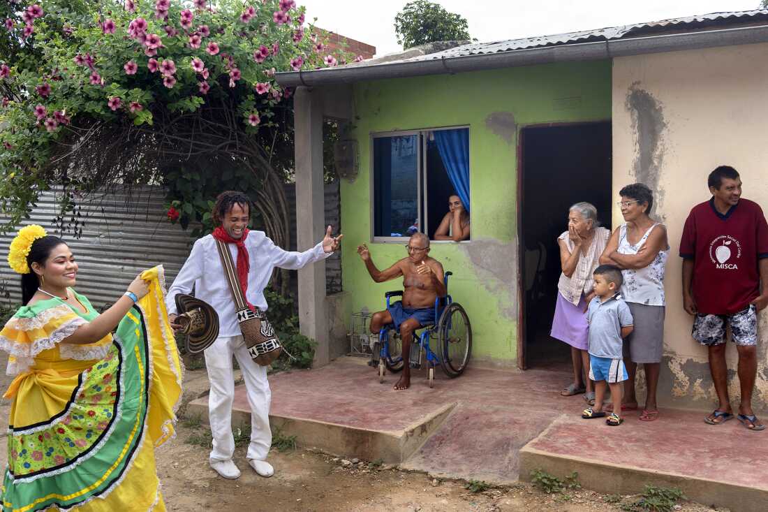 Melgen Melendez Baena, a cumbia dancer from Barranquilla, raises his hand as Cristobal Perez Santos, 72, watches from his wheelchair during a parade of gaitero groups and dancers in San Jacinto, Bolívar, Colombia, on August 14, 2022, at the Festival Nacional Autóctono de Gaitas. The gaita, a traditional cactus-made instrument, is <a href=