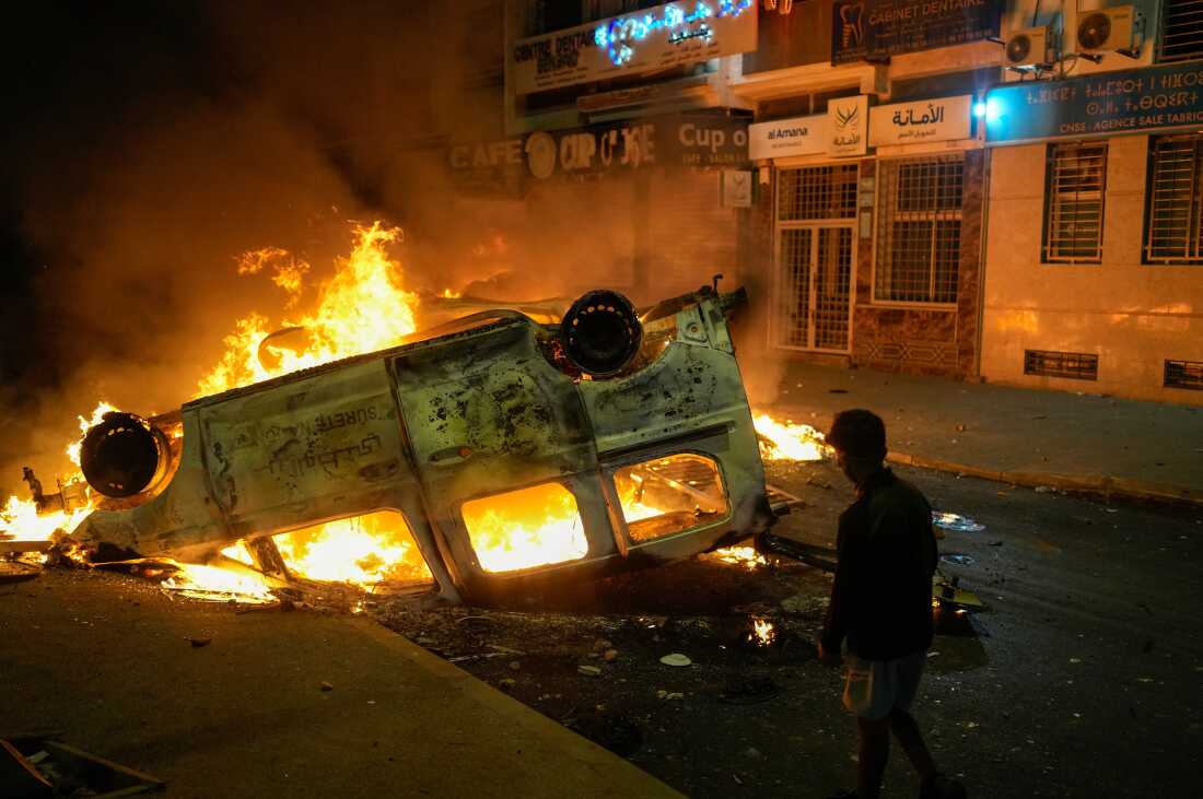 A young boy stands beside a burned police vehicle amid violent youth protests demanding reforms in Sale, Morocco.