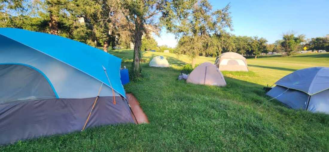 Numerous tents set up in a grassy area with trees in the background.
