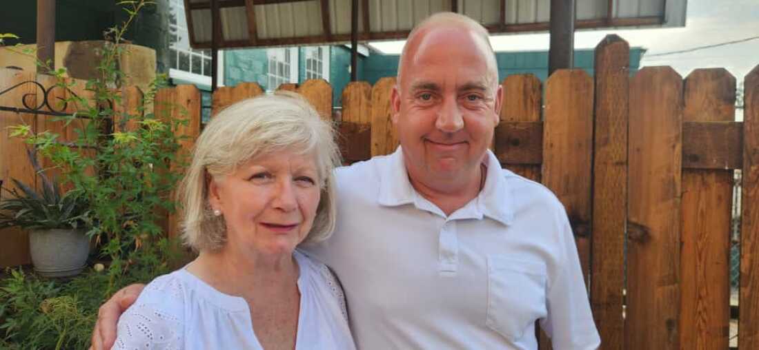 Judy Thompson and her son, Alton Aanderud, stand outdoors with a wooden fence behind them.