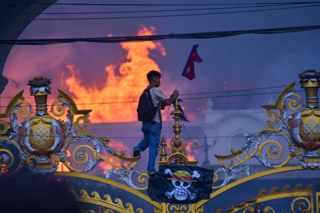 A man hangs a pirate flag as smoke and flames rise from the Singha Durbar, Nepal's government offices, Kathmandu, Sept. 9, 2025.
