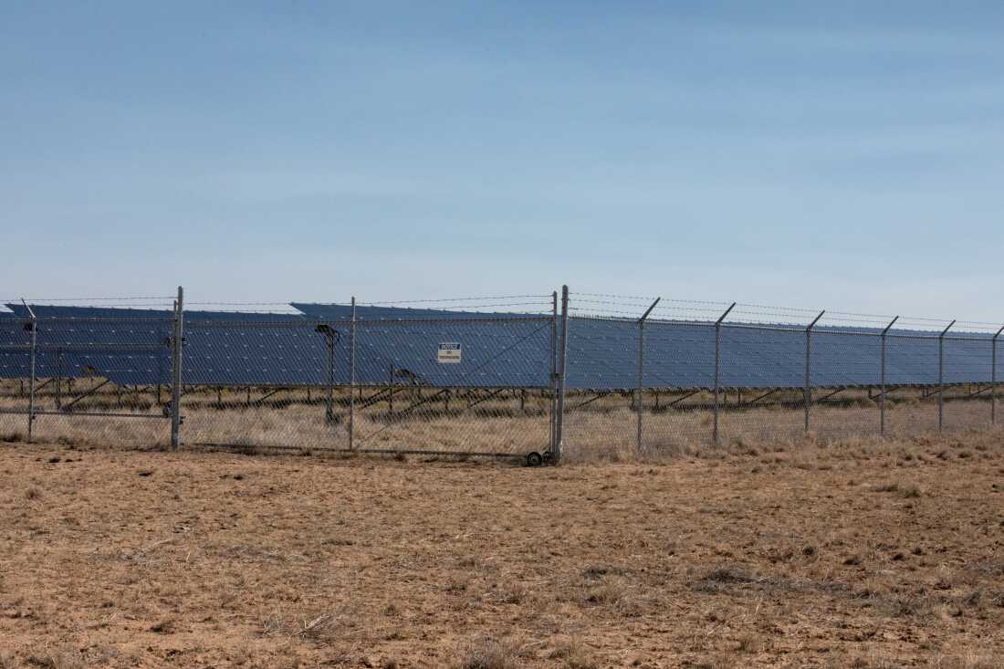 Solar panels behind a chain-link fence under a bright sky