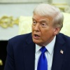 Wearing a navy blue suit and bright blue tie, President Trump speaks to reporters in the Oval Office on Tuesday while seated in a light yellow and gold upholstered chair.