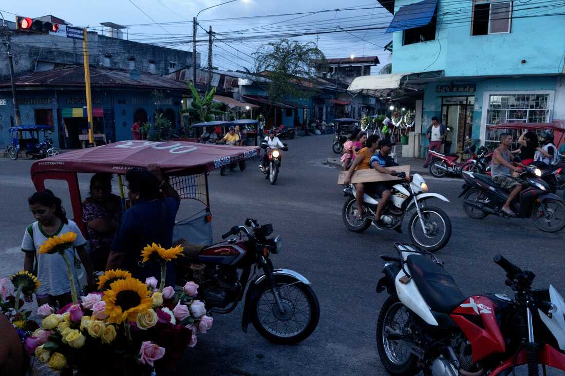 Flower vendors outside a cemetery in Iquitos, Peru, on October 28, 2024, as motorcycles pass by. Iquitos is home to Los Wembler's de Iquitos, pioneers of the cumbia Amazonica genre.