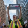 A protestor is holding a sign that says, 'End overdose deaths now.' There are very tall buildings on both sides of her and blue skies behind her.