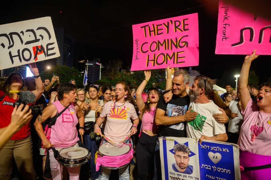 Michel Illouz and Ilan Dalal embrace during a rally in Hostages Square, Tel Aviv, with supporters holding signs reading 'they're <a href=