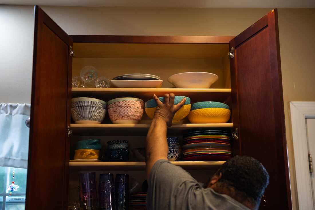Twitty grabs serving bowls from his kitchen cabinet. The cabinet is filled with colorful bowls and plates.