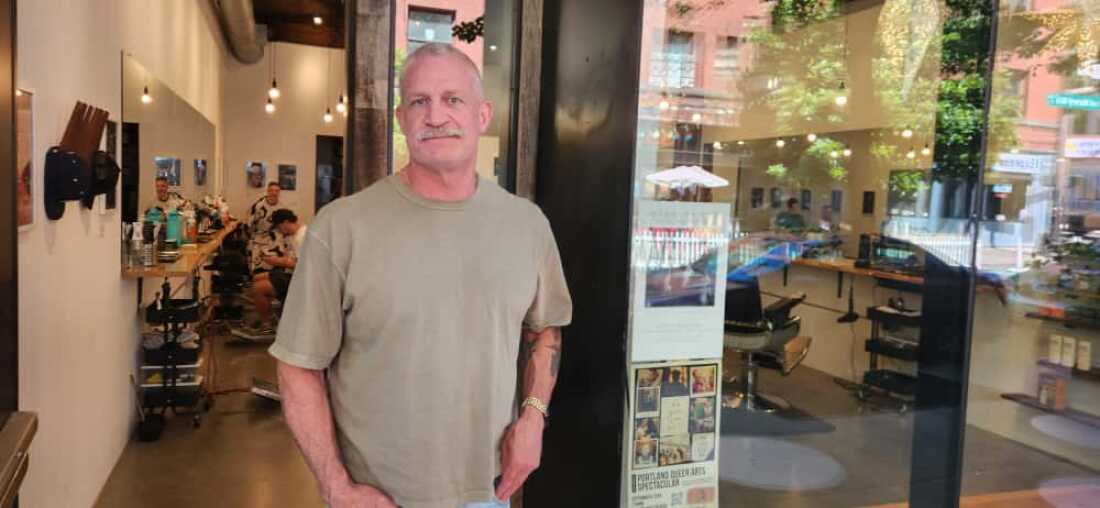 Logan Whalen stands in the doorway of the barbershop he runs in downtown Portland, Oregon.