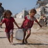 Displaced Palestinian girls carry water jerrycans after collecting supplies at a distribution point in a tent camp in Muwasi, a designated safe zone in southern Gaza's Khan Younis area.